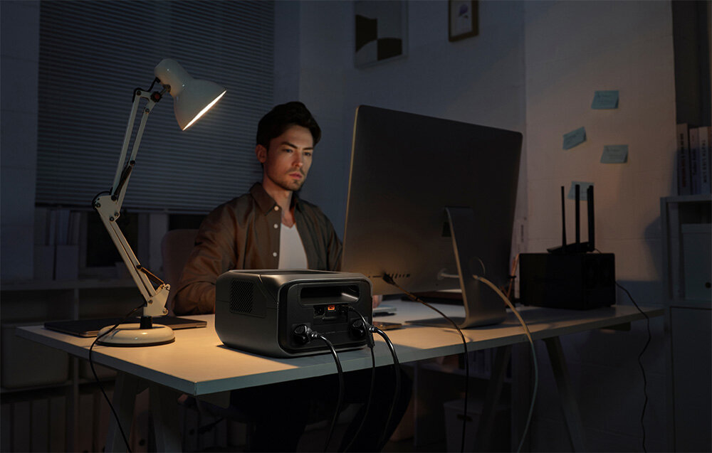 Stacja zasilania ECOFLOW River 3 Plus 286 Wh pokój osoba sidzie przy biurku na biurku stacja zasilania laptop i lampka wsparcie w różnych sytuacjach obsługuje urządzenia o mocy do 600 W funkcja X-Boost do 1200 W awaryjne zasilanie w niemal każdej sytuacji