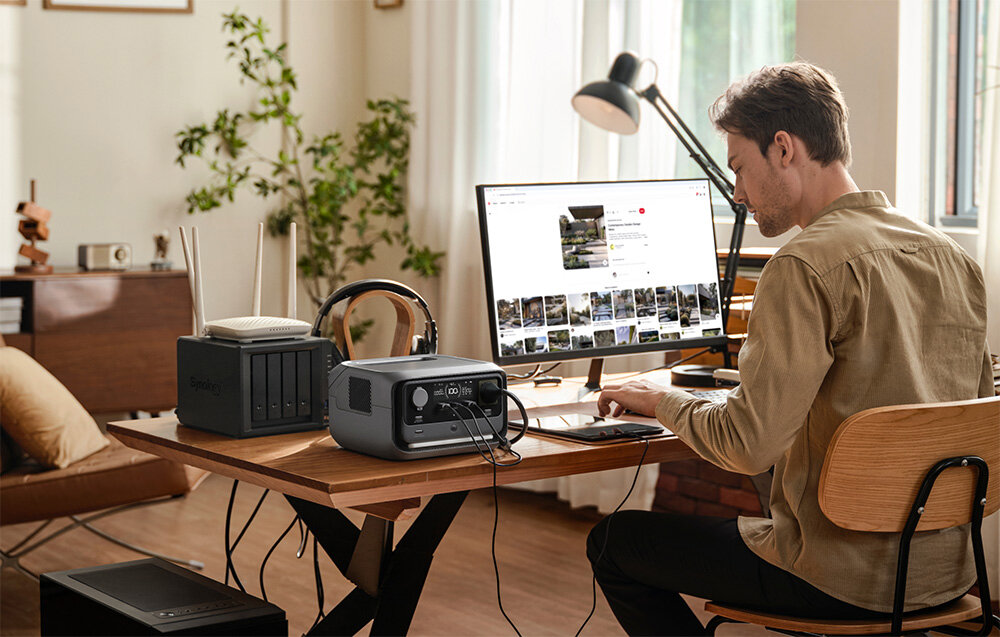 Stacja zasilania ECOFLOW River 3 Plus 286 Wh pokój osoba sidzie przy biurku na biurku stacja zasilania laptop i lampka bazowa pojemność 286 Wh akumulatora EB300 o pojemności 286 Wh lub akumulator EB600 oferującego 572 Wh technologia Pogo Pin nie musisz korzystać z kabli czy narzędzi oszczędność