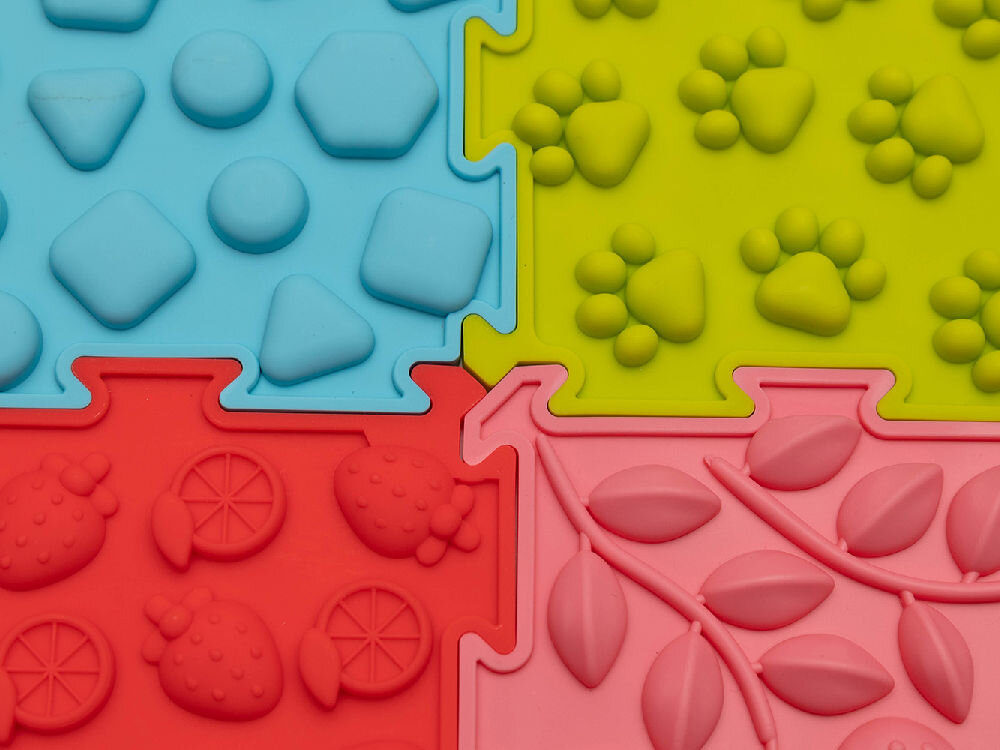 Mata sensoryczna ORTOPEDEK 128931 24.5 x 24.5 cm (8 elementów) WielokolorowyMata sensoryczna ORTOPEDEK 128931 24.5 x 24.5 cm (8 elementów) Wielokolorowy Makrofotografia pastelowego, różowego puzzla ortopedycznego Ortopedek. Zbliżenie pokazuje detale wypukłego wzoru w kształcie stóp z logotypem marki, służącego do stymulacji receptorów dotykowych.