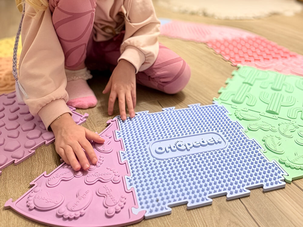 Mata sensoryczna ORTOPEDEK Zestaw mat 910152 (16 elementów) Dziecko bawi się na podłodze kolorowymi puzzlami sensorycznymi Ortopedek w pastelowych kolorach. Widoczne dłonie dotykające wypukłych faktur maty, w tym elementu z logo Ortopedek oraz puzzla z motywem stóp.
Plik 1.jpg