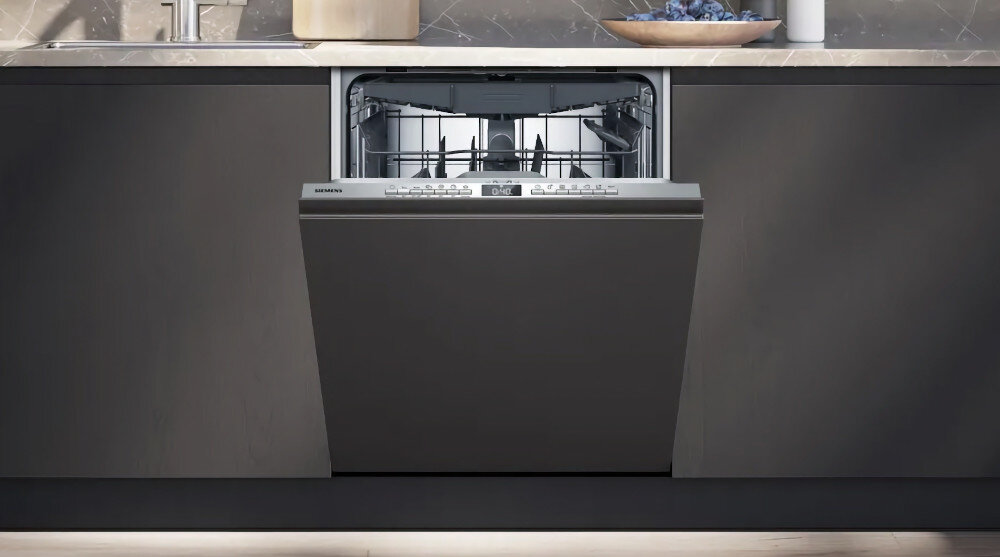 ZMYWARKA SIEMENS SN63EX03ME Zdjęcie przedstawia zmywarkę delikatnie uchyloną w zabudowie kuchennej, z eleganckim, ciemnym frontem. Wnętrze urządzenia jest widoczne jedynie w górnej części