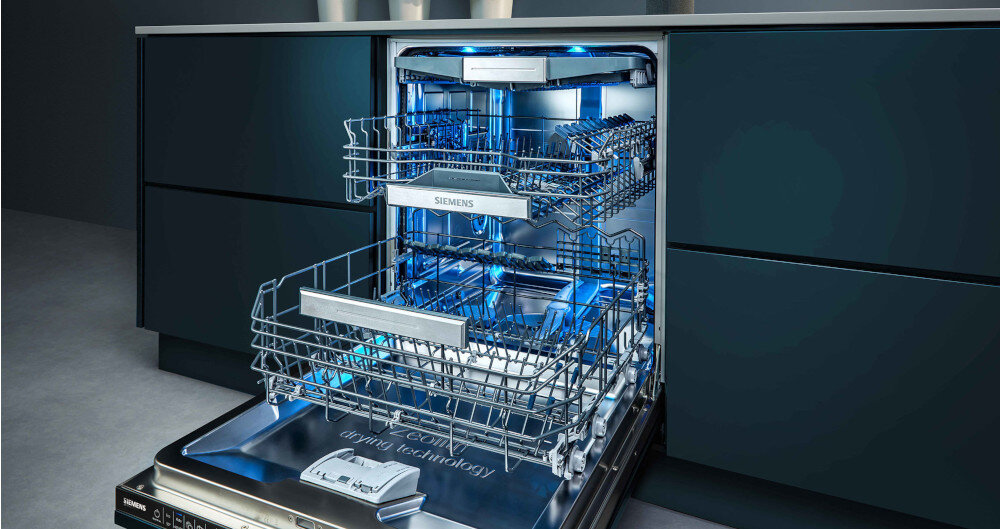ZMYWARKA SIEMENS SN63EX03ME Zdjęcie przedstawia otwartą zmywarkę Siemens z trzema poziomami koszy, oświetloną niebieskim światłem LED. Wnętrze wygląda bardzo przestronnie Machine Care czyszczenie zmywarki usuwanie osadów higiena urządzenia konserwacja wnętrza