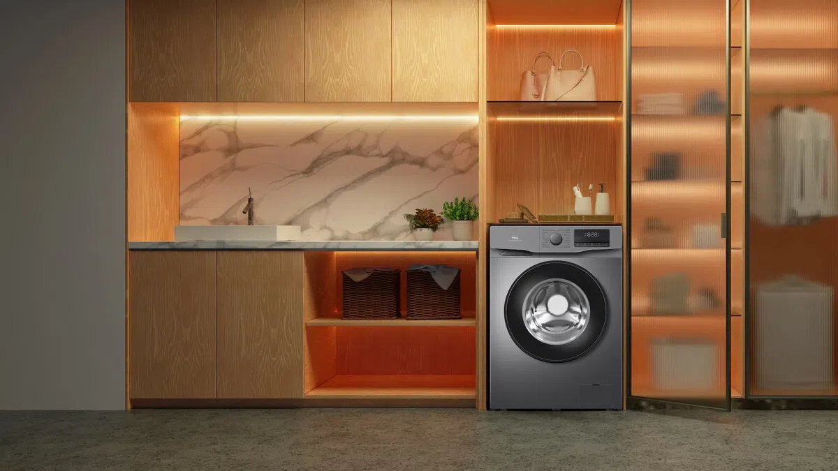 PRALKA TCL FF0612SB1PL Ciemna pralka wolnostojąca wkomponowana w zabudowę z czarnym blatem, otoczona wiszącą szafką z podświetlanymi półkami, rośliną w donicy, regałem oraz koszem na pranie, tworząca przytulną aranżację pralni energooszczędna inteligentne funkcje higieniczne pranie Steam Wash Auto Weight Honeycomb Drum czyste ubrania świeżość bezpieczeństwo komfort jakość