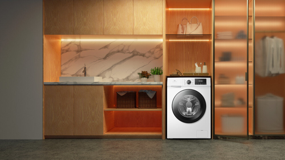 PRALKA TCL FF1024WA0PL Ciemna pralka wolnostojąca wkomponowana w zabudowę z czarnym blatem, otoczona wiszącą szafką z podświetlanymi półkami, rośliną w donicy, regałem oraz koszem na pranie, tworząca przytulną aranżację pralni energooszczędna inteligentne funkcje higieniczne pranie Steam Wash Auto Weight Honeycomb Drum czyste ubrania świeżość bezpieczeństwo komfort jakość