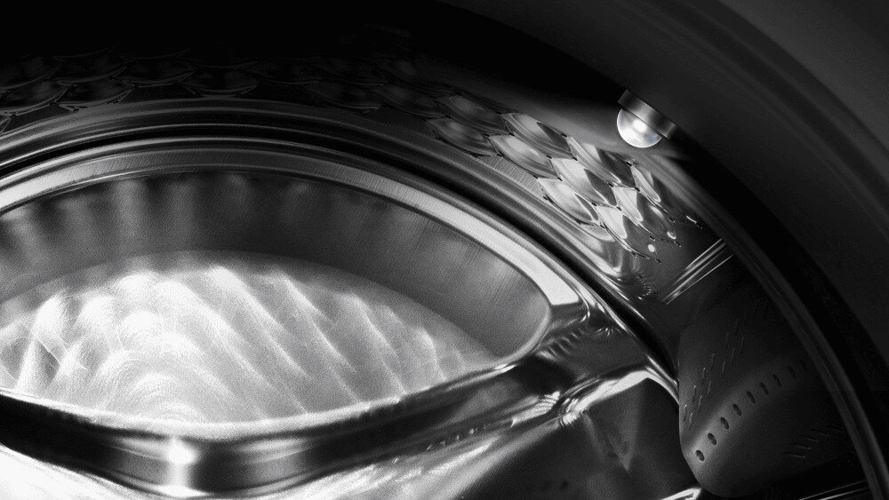 PRALKA TCL FP0834WA1PL Zbliżenie wnętrza bębna pralki w czarno-białej tonacji z włączonym punktowym oświetleniem LED, które rozjaśnia metalową powierzchnię i ułatwia kontrolę zawartości oświetlenie bębna kontrola zawartości wygoda prania lepsza widoczność