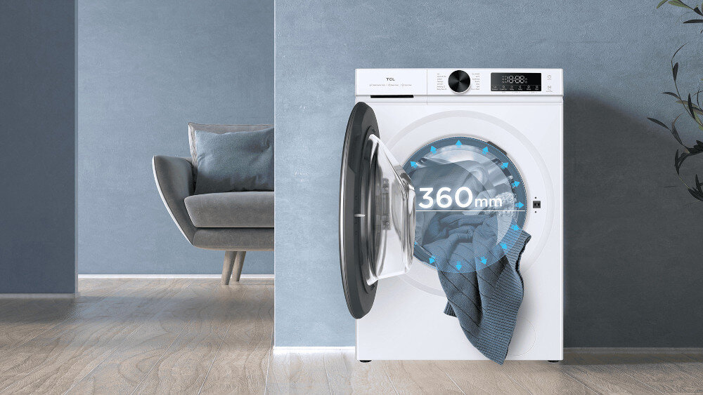 PRALKA TCL FP0944WA0PL W niebiesko‑szarym wnętrzu stoi pralko‑suszarka TCL z otwartymi drzwiami, z których wysuwa się koc, a na przeszklonym froncie wyeksponowano napis „360 mm” oraz niebieski pierścień strzałek, podkreślający szeroki otwór załadunkowy ułatwiający wkładanie i wyjmowanie prania Mega Opening Mega Door szerokie drzwi duży załadunek koce pościel wygoda prania łatwe wkładanie solidna konstrukcja
