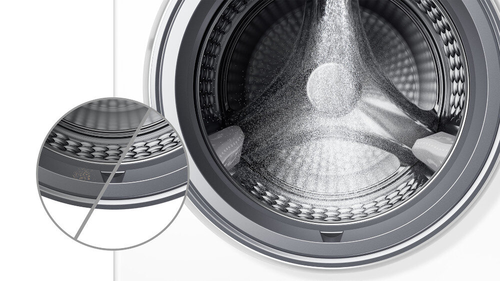 PRALKA TCL FP0944WA0PL Zbliżenie wnętrza bębna pralki pokazuje strumień wody lub detergentu rozprowadzany po ściankach bębna o strukturze „plastra miodu”, a w powiększonym kole po lewej wyróżniono gładkie krawędzie otworów, które mają delikatnie obchodzić się z tkaninami Spray Wash czysty bęben usuwanie resztek detergentu zabrudzenia konserwacja pralki dłuższa żywotność higiena urządzenia