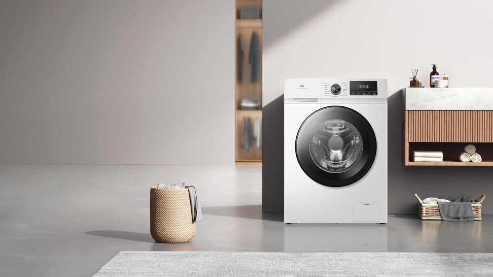 PRALKA TCL FF0924WA0PL Na drugim zdjęciu pralka jest centralnie umieszczona w nowoczesnej zabudowie z szarymi frontami i czarnym blatem, pełniąc rolę głównego elementu strefy pralni. Nad blatem znajduje się podświetlana szafka z półkami na kosmetyki i detergenty oraz dekoracje, a po prawej stronie widoczny jest regał i duża roślina doniczkowa na drewnianej podłodze energooszczędność cicha praca inteligentne technologie komfort
