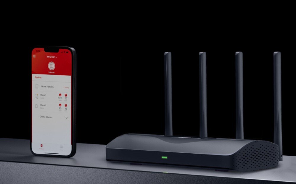 Router MERCUSYS MR27BE Smartfon wyświetlający interfejs aplikacji do zarządzania siecią stojący obok routera na ciemnym blacie