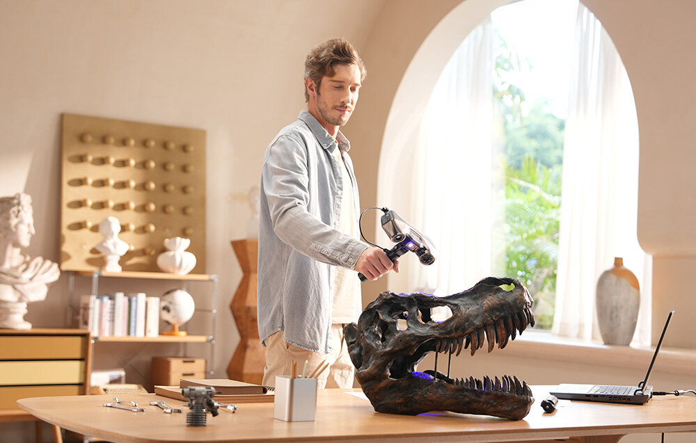 Mężczyzna wykonujący ręczny skan 3D dużej repliki czaszki dinozaura za pomocą skanera Revopoint MetroY Pro