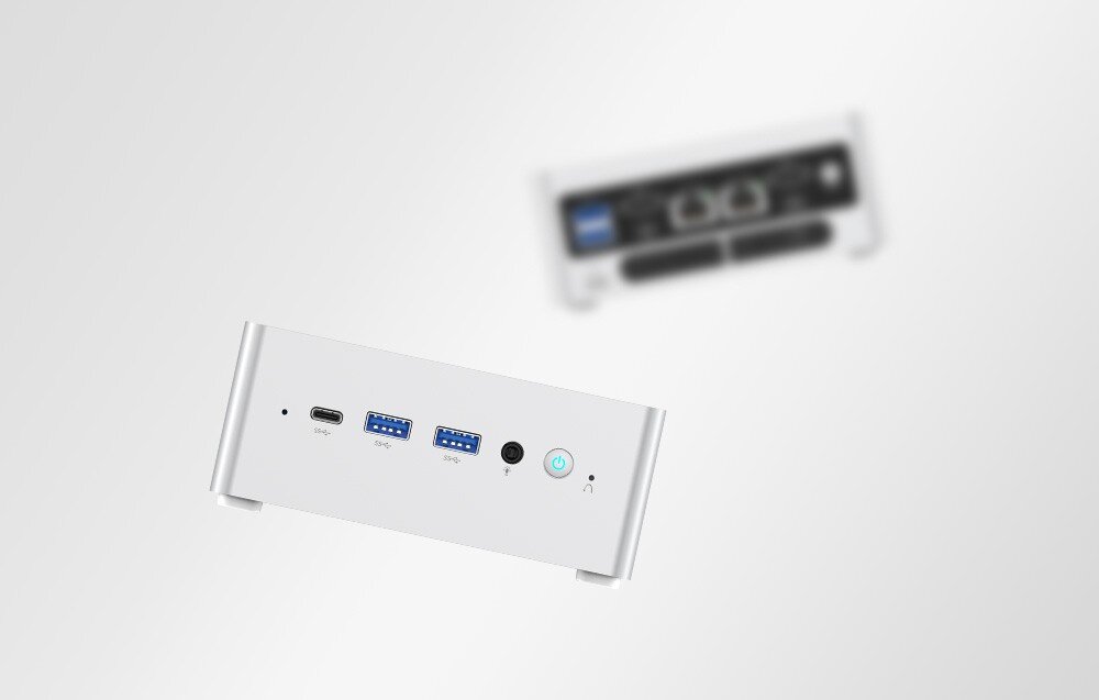 Komputer MINISFORUM NAB6 Lite Przedni panel mini PC na pierwszym planie, w tle rozmazany widok tylnego panelu z gniazdami sieciowymi.