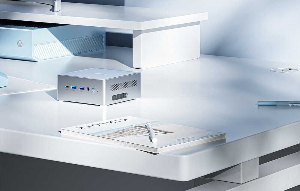 Komputer MINISFORUM NAB6 Lite Mały komputer ustawiony na białym biurku pod półką z konsolą do gier