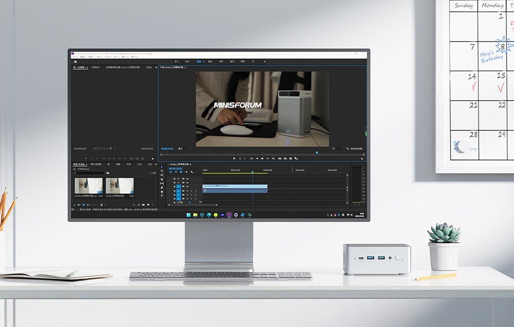Komputer MINISFORUM NAB6 Lite Monitor wyświetla program do montażu wideo, a mały komputer stoi na biurku obok rośliny i kalendarza