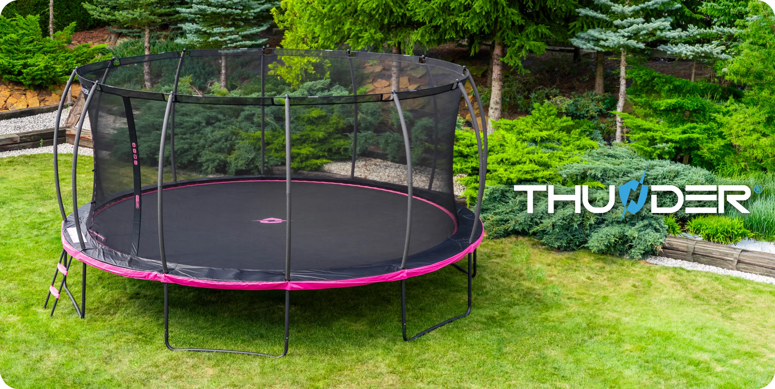 Na obrazie widoczna jest duża trampolina ogrodowa z siatką ochronną i drabinką, umieszczona na trawniku w otoczeniu zieleni. W prawym dolnym rogu znajduje się logo z napisem \'THUNDER\'.