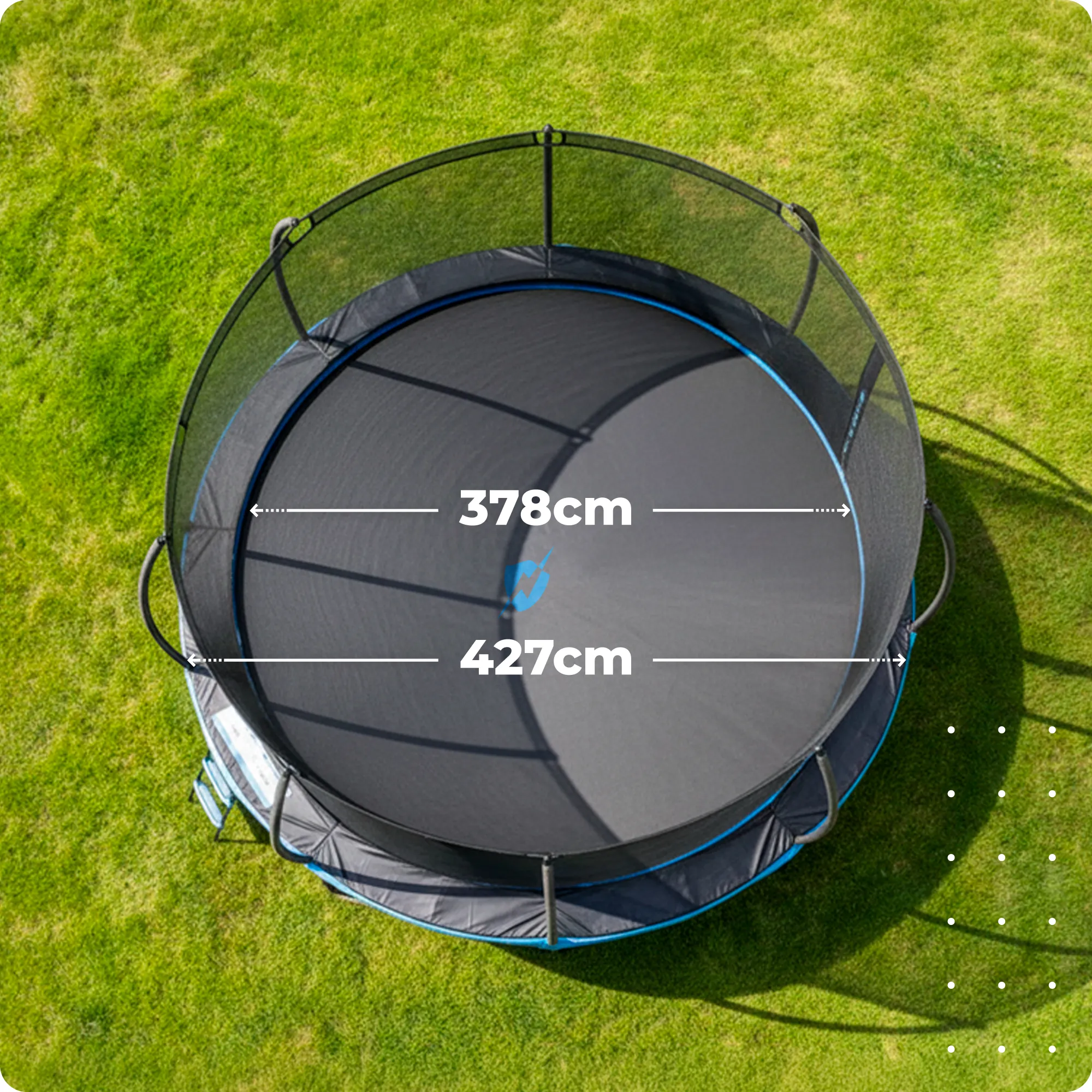 Na obrazie widoczna jest duża trampolina ogrodowa z siatką ochronną, umieszczona na trawie. Na trampolinie znajdują się oznaczenia \'324cm\' i \'366cm\'.