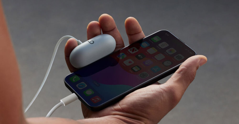 Słuchawki dokanałowe BEATS Solo Buds bateria 18 godzin, Fast Fuel 5 minut ładowania, ładowanie mobilne, osoba trzymająca telefon oraz etui ładujące w ręku połączone kablem do ładowania
