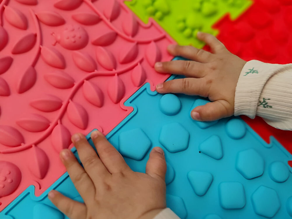 Mata sensoryczna ORTOPEDEK 128948 24.5 x 24.5 cm (12 elementów) Wielokolorowy Perspektywiczny widok na zestaw mat sensorycznych Ortopedek ułożonych w duży pierścień na białym tle. Wielokolorowe puzzle ortopedyczne w pastelowych odcieniach przeznaczone do ćwiczeń korekcyjnych i zabawy.