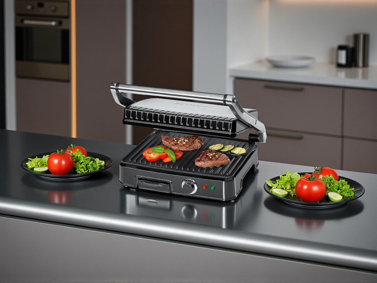 Grill elektryczny BOMANN KG 2242 CB, smażenie, gotowanie, grillowanie, jedzenie, Grill elektryczny BOMANN KG 2242 CB z zamkniętą, stalową pokrywą, ustawiony na blacie kuchennym w jasnej nowoczesnej kuchni, obok talerza z warzywami.