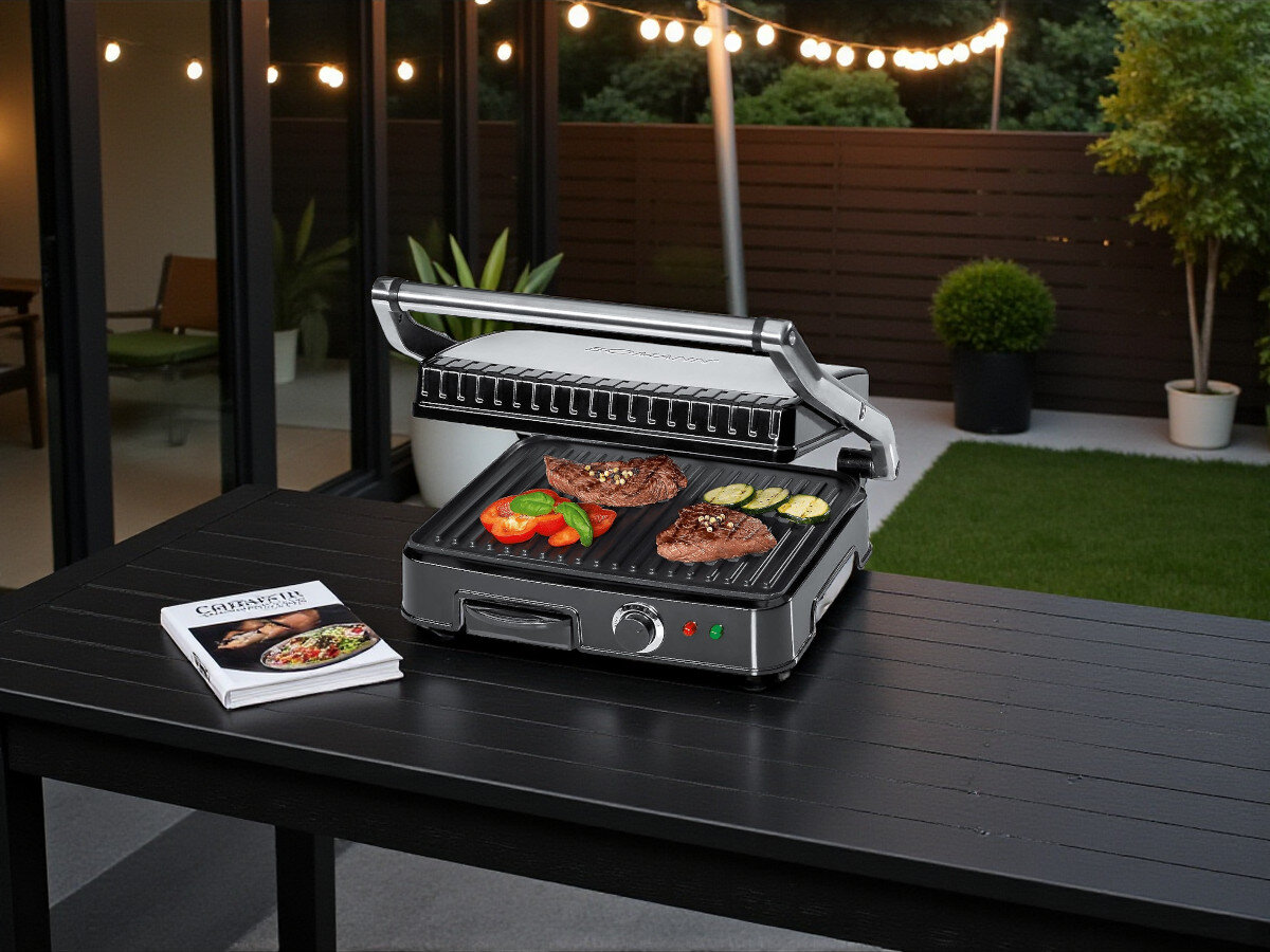 Grill elektryczny BOMANN KG 2242 CB, nagrzewanie, potrawy, nierdzewna, wnęka, Otwarty grill BOMANN KG 2242 CB w kuchni, na płytach grzewczych stek, papryka i cukinia, obok dwie czarne talerze z pomidorami i sałatą.