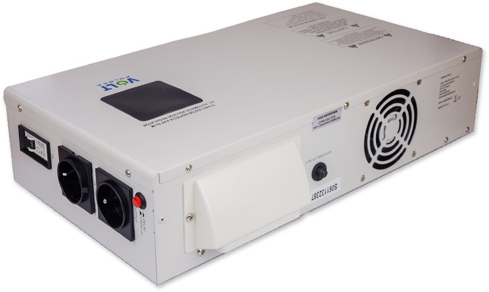 Stabilizator napięcia VOLT AVR Biała metalowa obudowa urządzenia elektronicznego widoczna z ukosa, prezentująca górny panel z czarnym ekranem i naklejkami ostrzegawczymi oraz bok z otworami wentylacyjnymi i gniazdem wyjściowym