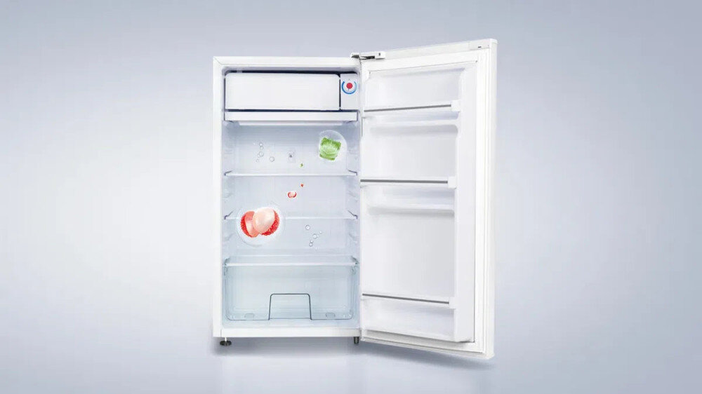 LODÓWKA TCL RF092DWE0 Na grafice pokazano otwartą, białą chłodziarkę jednodrzwiową z małą zamrażarką u góry, trzema szklanymi półkami oraz transparentną szufladą na warzywa na dole. Na niemal pustych półkach widać tylko kilka owoców i kostek lodu, co podkreśla gładkie, łatwe do czyszczenia wnętrze z tworzywa HIPS wnętrze HIPS odporność na zarysowania łatwe czyszczenie gładka powierzchnia higiena lodówki ochrona przed bakteriami brak pochłaniania zapachów bezpieczne przechowywanie żywności