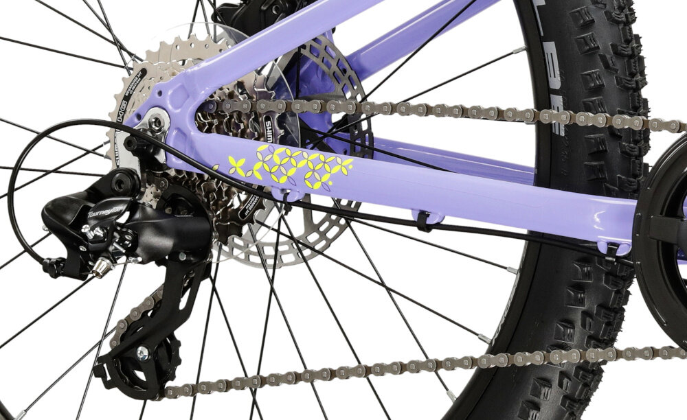 Zbliżenie na tylną część roweru z fioletową ramą i widocznym mechanizmem przerzutki oraz hamulcem tarczowym. Na ramie znajduje się żółty napis \'KROSS\'.