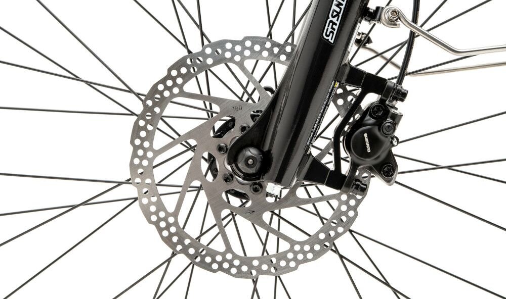 Zbliżenie na tarczę hamulcową roweru z widocznym zaciskiem i szprychami koła. Na widocznej części widnieje napis \'SHIMANO\'.