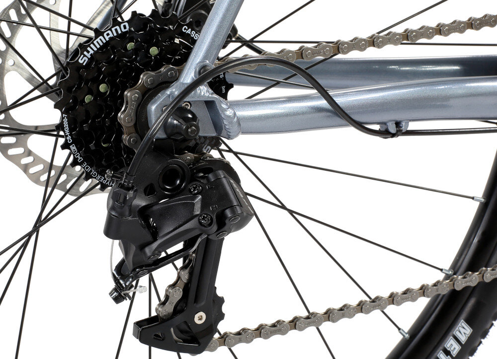 Zdjęcie przedstawia tylną część roweru z widocznym mechanizmem przerzutki i kasetą zębatek. Na kasetach widoczny jest napis \'SHIMANO\'.