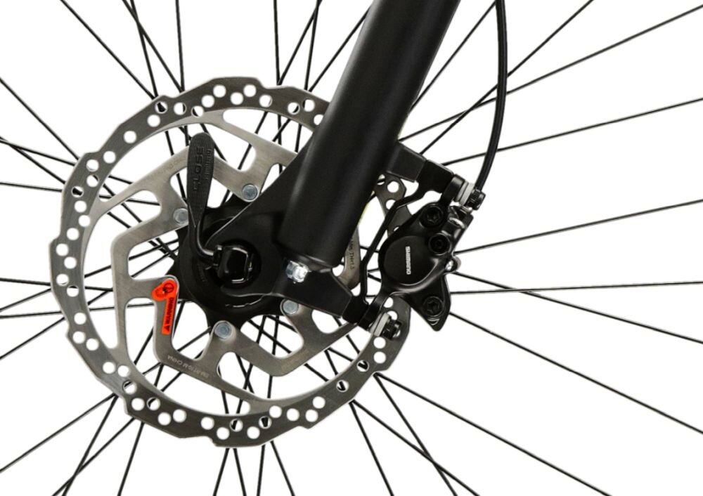 Zdjęcie przedstawia tarczę hamulcową roweru z widocznym zaciskiem hamulcowym i szprychami koła. Na zacisku widoczny jest napis \'SHIMANO\'.