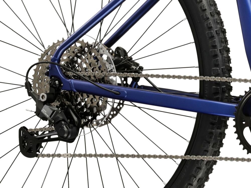 Zdjęcie przedstawia tylne koło roweru z widocznym mechanizmem przerzutki i łańcuchem. Na ramie roweru widoczny jest napis \'E-MTB 4.0\'.