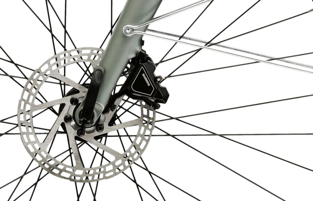 Zbliżenie na tarczę hamulcową roweru z widocznym zaciskiem hamulcowym marki Shimano. W tle widać szprychy koła.