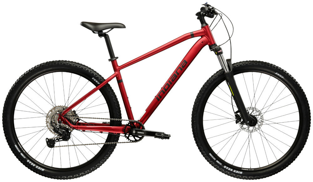 Rower górski MTB INDIANA X-Pulser 3.9 M20 29 cali męski Rubinowo-czarny droga gruntowa osoba w kasku jedzie po drodze gruntowej w tle łąka niebieskie niebo pasja jazda na rowerze środek transportu