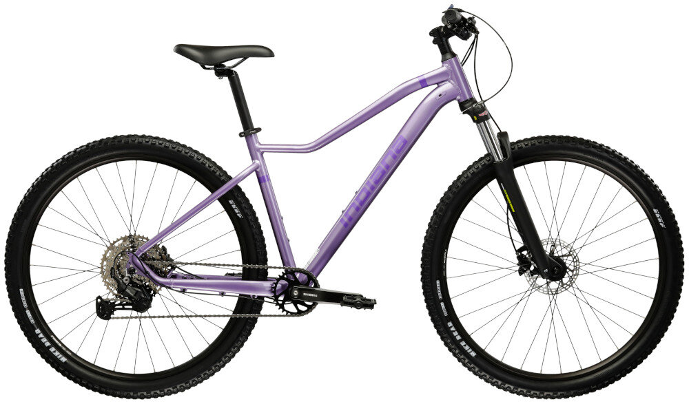Rower górski MTB INDIANA X-Pulser 3.9 D18 29 cali damski Lawendowo-fioletowy droga gruntowa osoba w kasku jedzie po drodze gruntowej w tle łąka niebieskie niebo pasja jazda na rowerze środek transportu