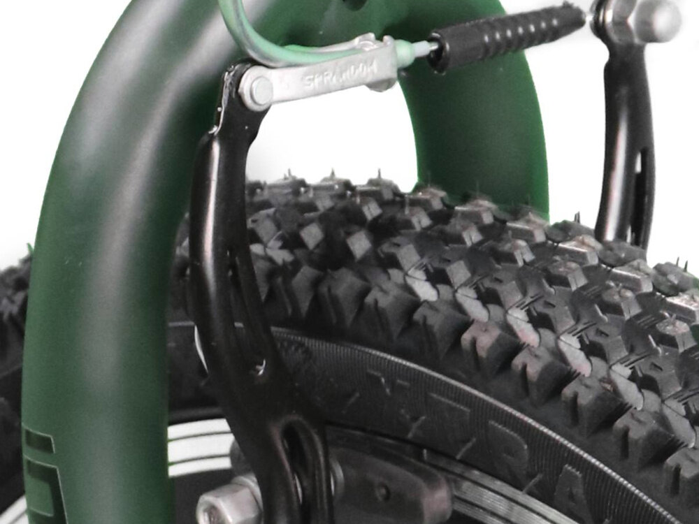 Zbliżenie na oponę roweru z wyraźnym bieżnikiem oraz fragmentem zielonego błotnika. Widoczny jest element hamulca z napisem \'SP RIM\'.