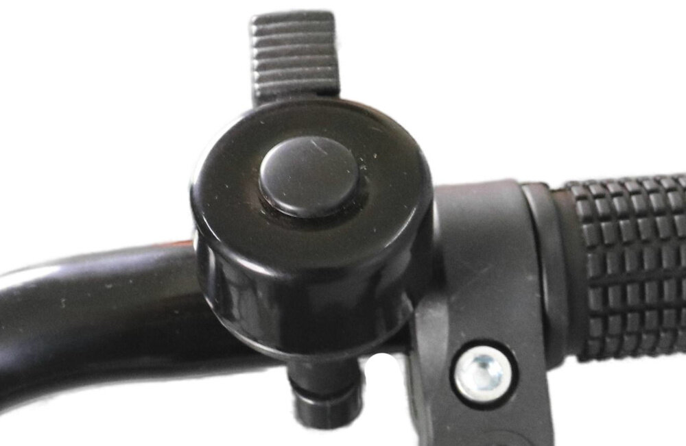 Zbliżenie na czarny dzwonek rowerowy zamontowany na kierownicy z gumowym uchwytem. Widoczna jest również śruba mocująca dzwonek do kierownicy.