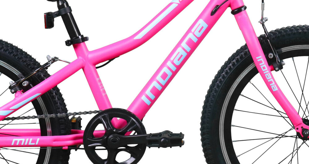 Różowy rower dziecięcy z białymi napisami \'INDIANA\' na ramie i \'MILI\' na dolnej rurze. Widoczne są czarne opony z grubym bieżnikiem oraz mechanizm korbowy.
