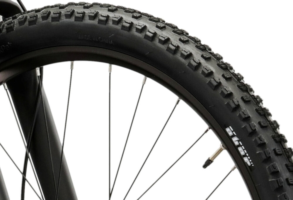 Zbliżenie na oponę rowerową z wyraźnym bieżnikiem i widocznymi szprychami. Na oponie widoczny jest tekst: \'MADE IN CHINA\'.