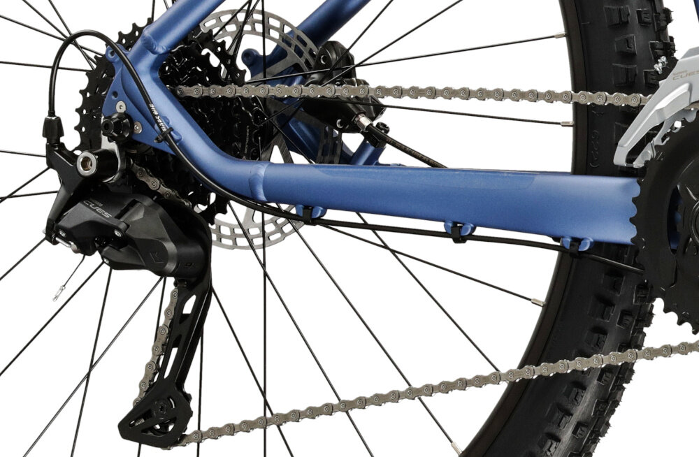 Zbliżenie na tylną część roweru górskiego z widocznym mechanizmem przerzutki, łańcuchem i tarczą hamulcową. Rama roweru jest w kolorze niebieskim, a opona ma wyraźny bieżnik.