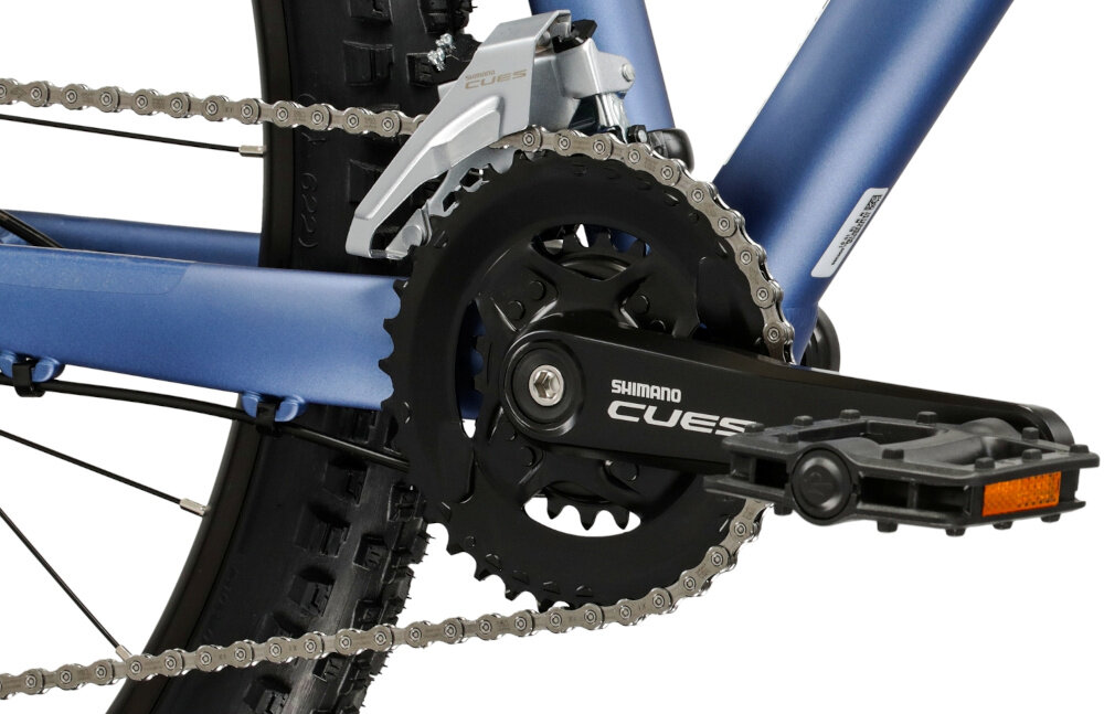 Zbliżenie na mechanizm korbowy roweru z widocznym napisem \'SHIMANO CUES\'. Łańcuch jest zamontowany na zębatce, a rama roweru ma niebieski kolor.