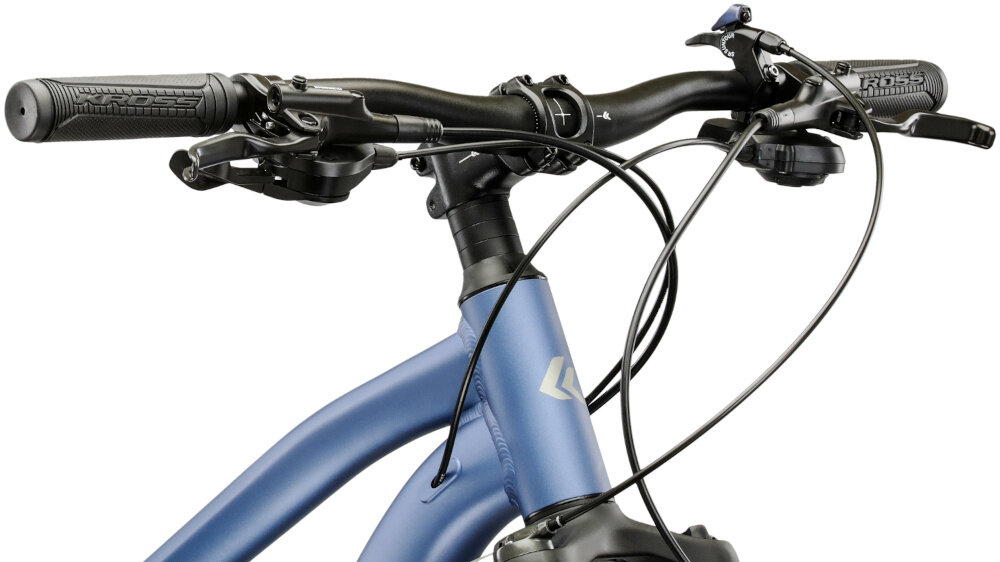 Zbliżenie na kierownicę roweru górskiego z widocznymi manetkami i przewodami hamulcowymi. Rama roweru jest w kolorze niebiesko-szarym z logo producenta na rurze sterowej.