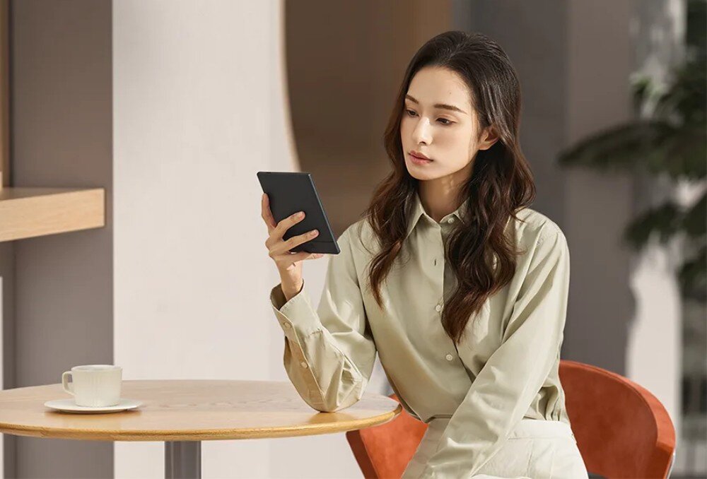 Czytnik e-booków ONYX BOOX Go Kobieta siedząca przy okrągłym stole w kawiarni, trzymająca w dłoni elektroniczne urządzenie do czytania, kompatybilność, formaty plików
