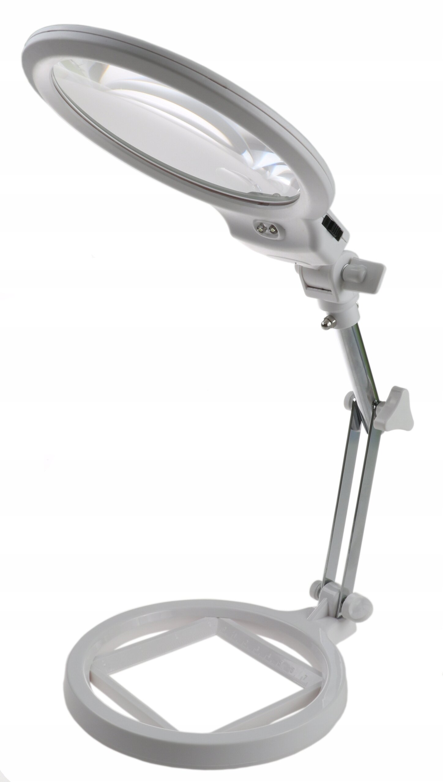 Biała lampa LED z wbudowanym szkłem powiększającym, zamocowana na regulowanym ramieniu. Podstawa lampy jest okrągła z kwadratowym otworem pośrodku.
