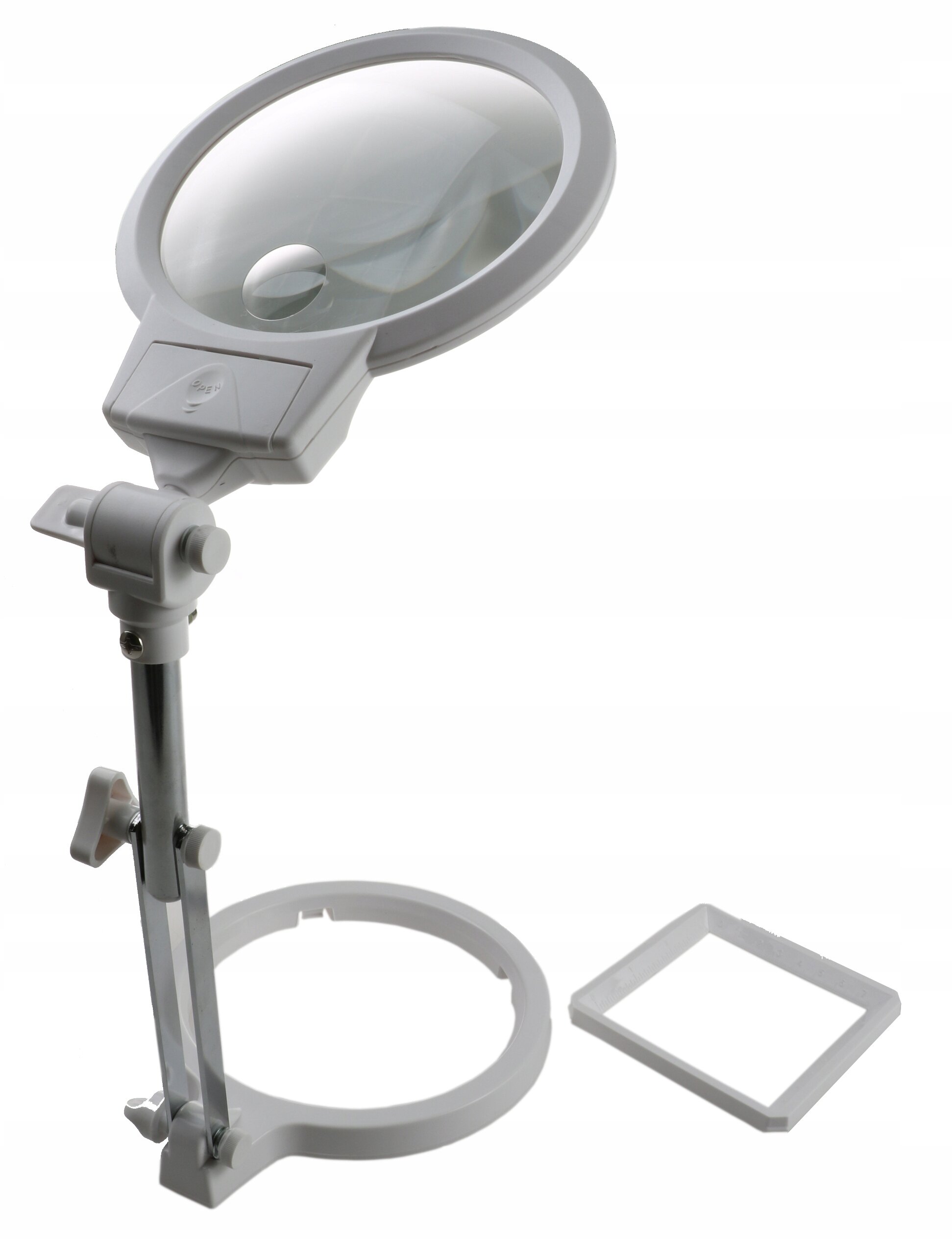 Na obrazie widoczna jest lampa LED z lupą na regulowanym stojaku, wykonana z białego tworzywa. Obok znajduje się kwadratowa ramka, prawdopodobnie część zestawu.