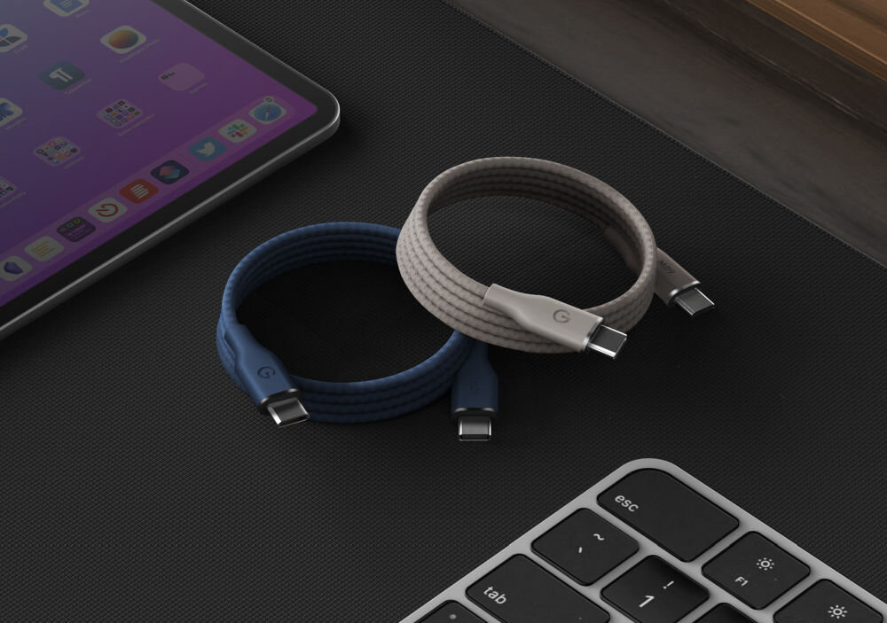 Na obrazie znajdują się dwa zrolowane kable USB-C w kolorach niebieskim i szarym, leżące obok tabletu i klawiatury. Na końcówkach kabli widoczne jest logo w kształcie litery \'G\'.