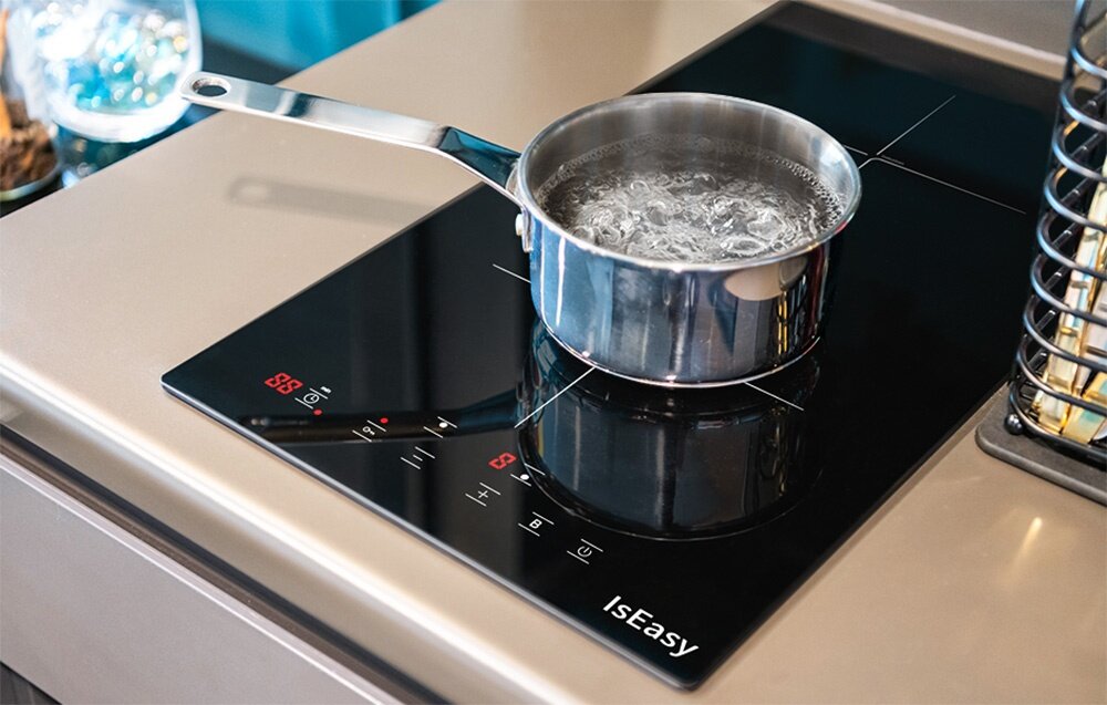 Płyta indukcyjna ISEASY LI2V-22 Na płycie indukcyjnej stoi garnek z gotującą się wodą, a cyfrowy panel wyświetla ustawienia. Ujęcie pokazuje energiczne wrzenie w naczyniu technologia indukcyjna energooszczędne szybkie gotowanie moc 1800 2000 W wysoka wydajność efektywność oszczędność energii