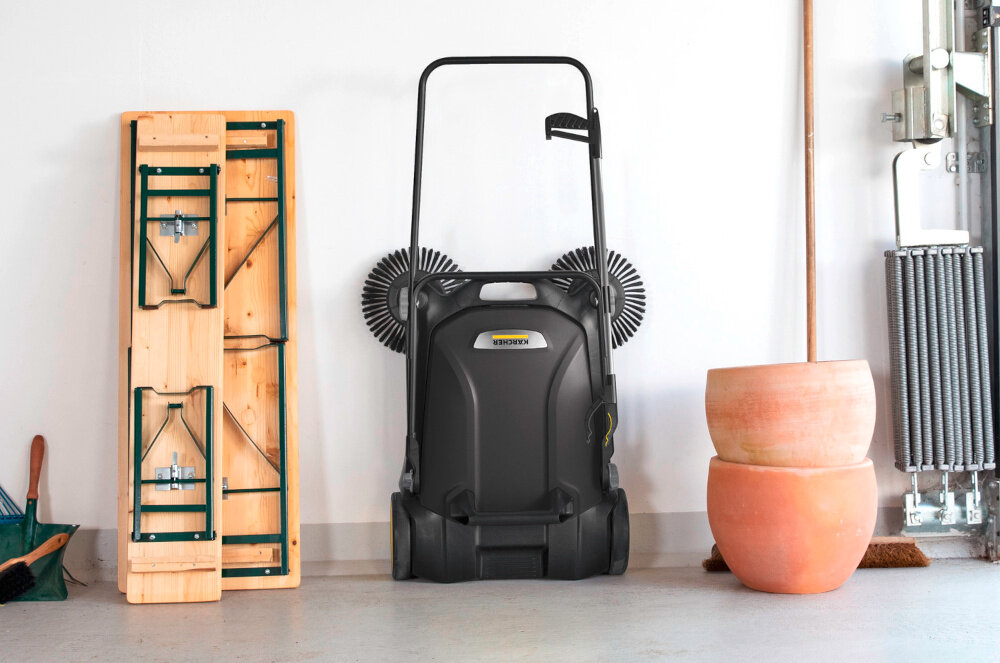 Zamiatarka KARCHER S 4 Twin Go Further 1.766-363.0 garaż złożona zamiatarka stoi oparta o ścianę obok złożona ławka doniczki narzędzia ręczne szybkie sprzątanie porządek wszechstronne zastosowanie