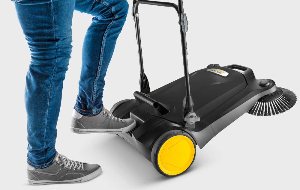 Zamiatarka KARCHER S 4 Twin Go Further 1.766-363.0 osoba przykłada stopę do uchwytu nożnego białe tło uchwyt nożny umożliwia złożenie urządzenia bez schylania się dodatkowy uchwyt transportowy ułatwia przenoszenie zamiatarki