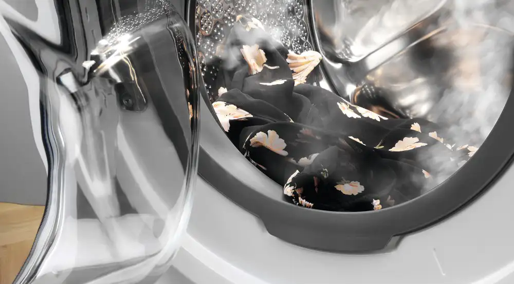 Wnetrze otwartej pralki z fragmentem sukienki o parą.