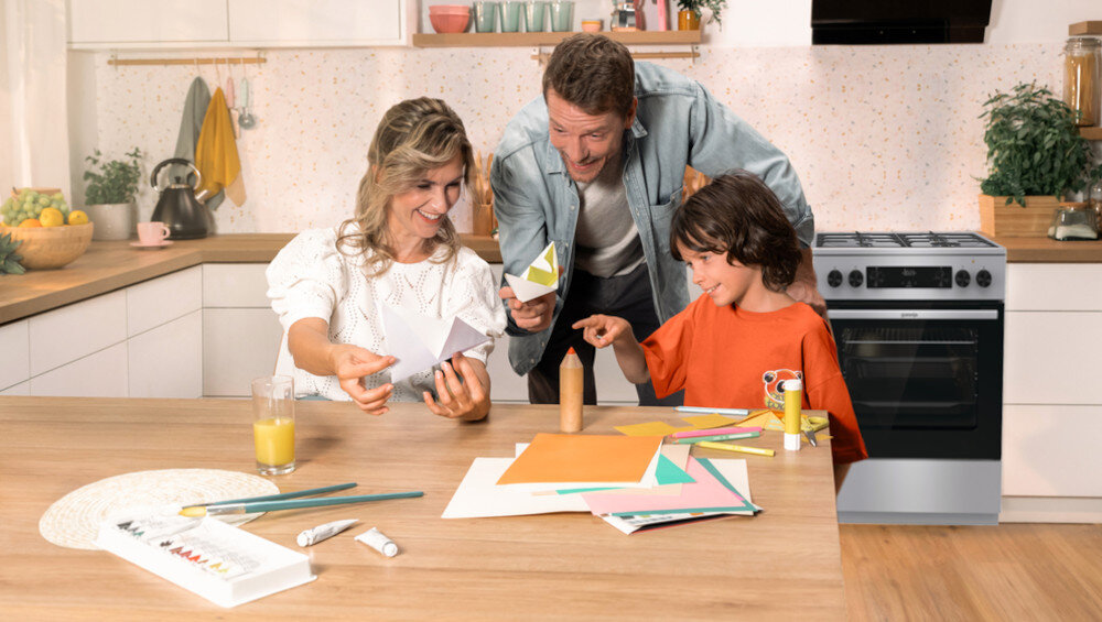 KUCHNIA GORENJE GK5C65XV lifestyle kuchnia rodzina dziecko akcesoria plastyczne na stole kuchenka w tle kolor czarno srebrny okap półki czajnik akcesoria kuchenne na blacie