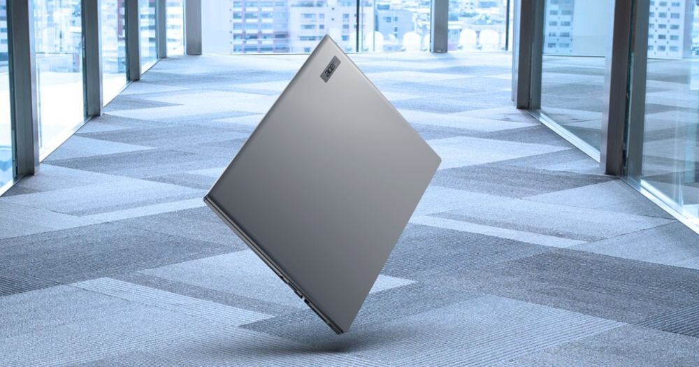 Laptop w kolorze srebrnym unosi się nad podłogą w nowoczesnym wnętrzu z dużymi oknami. Na obudowie widoczne jest logo \'ACER\'.